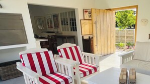 A patio area with white and red striped chairs, a white table, and a wooden door leading to a garden. - Dune • has a pool • 600m to Beach Robberg 5 (Plettenberg Bay)
