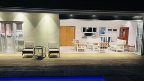 A poolside area with a wooden deck, a pool with blue lighting, and a seating area with white furniture. - Dune • has a pool • 600m to Beach Robberg 5 (Plettenberg Bay)