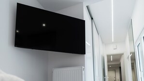 Ein modernes Hotelzimmer mit einem an der Wand befestigten Flachbildfernseher, einem ordentlich gefalteten weißen Handtuch auf dem Bett und Blick auf den Flur zum Badezimmer.