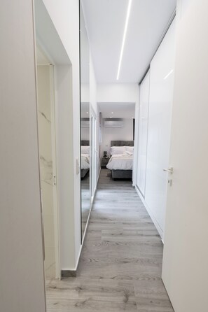 A narrow hallway with a wooden floor leading to a bedroom with a bed and a nightstand. - Charming 2 Bedroom House in Iraklio, Greece (Irakleio)