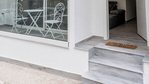 Ein modernes Gebäude mit Glastür, einem Balkon mit Metallstühlen und einer sichtbaren Innentreppe.