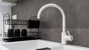 Eine moderne Küche mit einem weißen Spülbecken, einem schwarzen Drahtgestell mit Tassen und einer grauen Spritzschutzwand.