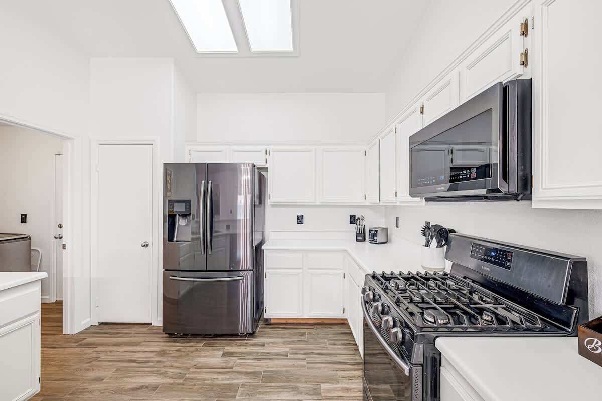 A modern kitchen with white cabinetry, a stainless steel refrigerator, a gas stove, and a microwave.