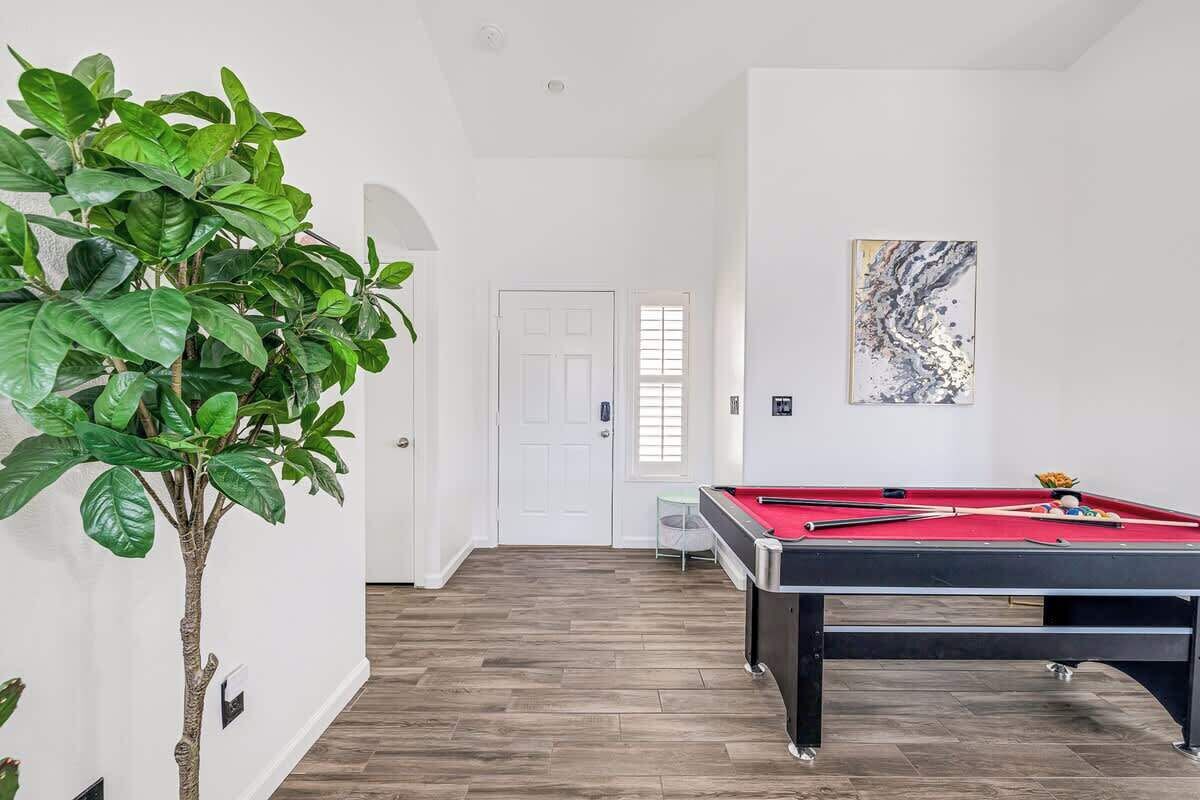 Une pièce avec une table de billard, une plante en pot et une porte donnant sur une autre pièce.
