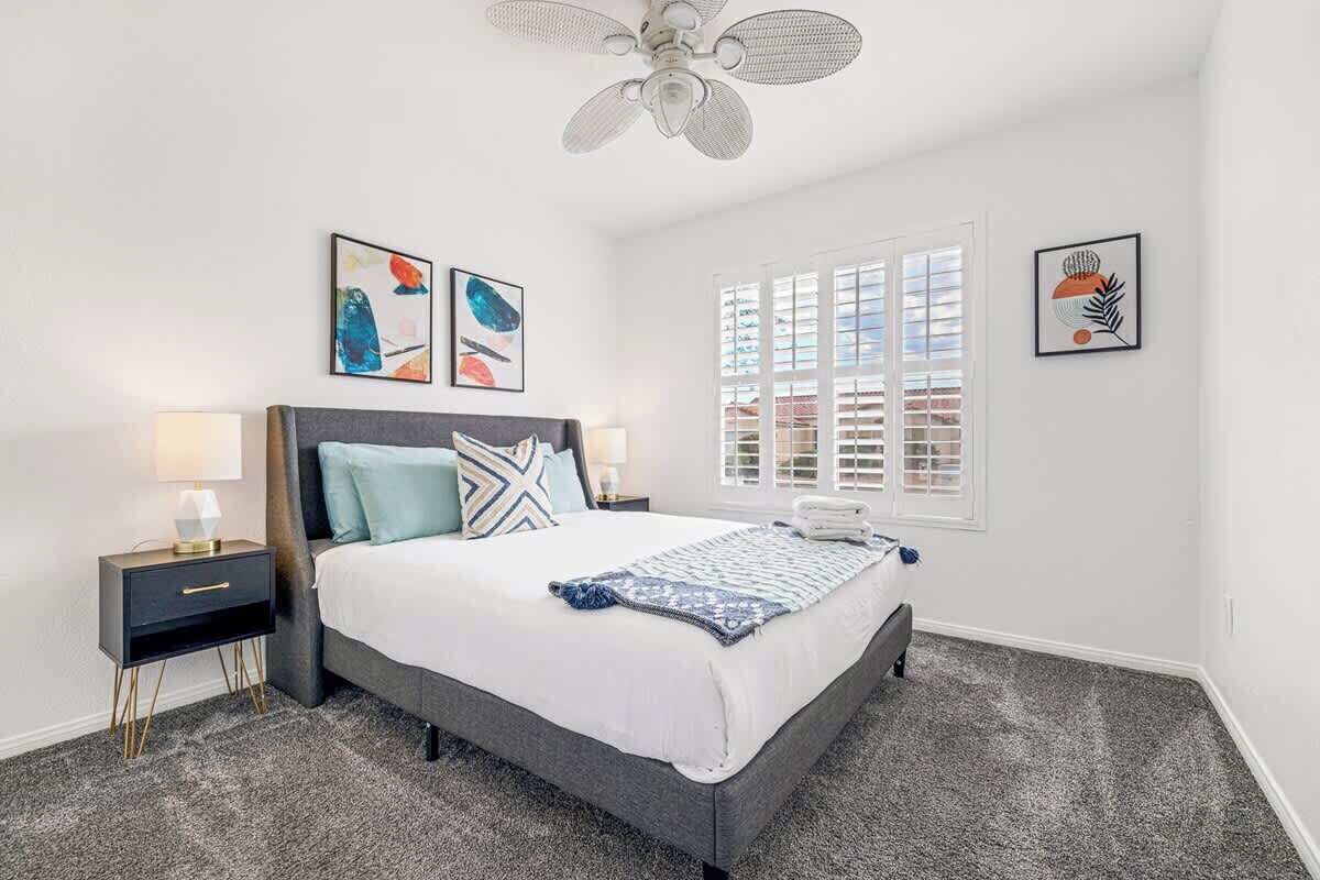 A bedroom with a bed, nightstands, a ceiling fan, and artwork on the walls.