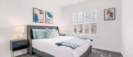 A bedroom with a bed, nightstands, a ceiling fan, and artwork on the walls.