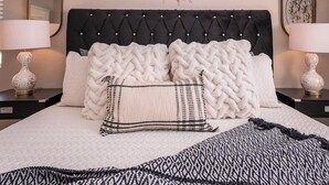 A neatly made bed with a tufted headboard, two bedside tables with lamps, and decorative mirrors on the walls. - Spacious Yard+Pool Table at 5BR Modern Getaway (North Las Vegas)