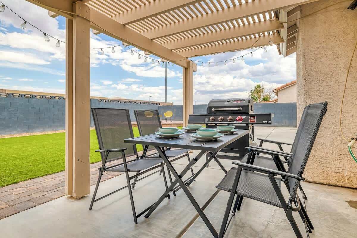 Een terras buiten met een barbecue, eettafel en stoelen.