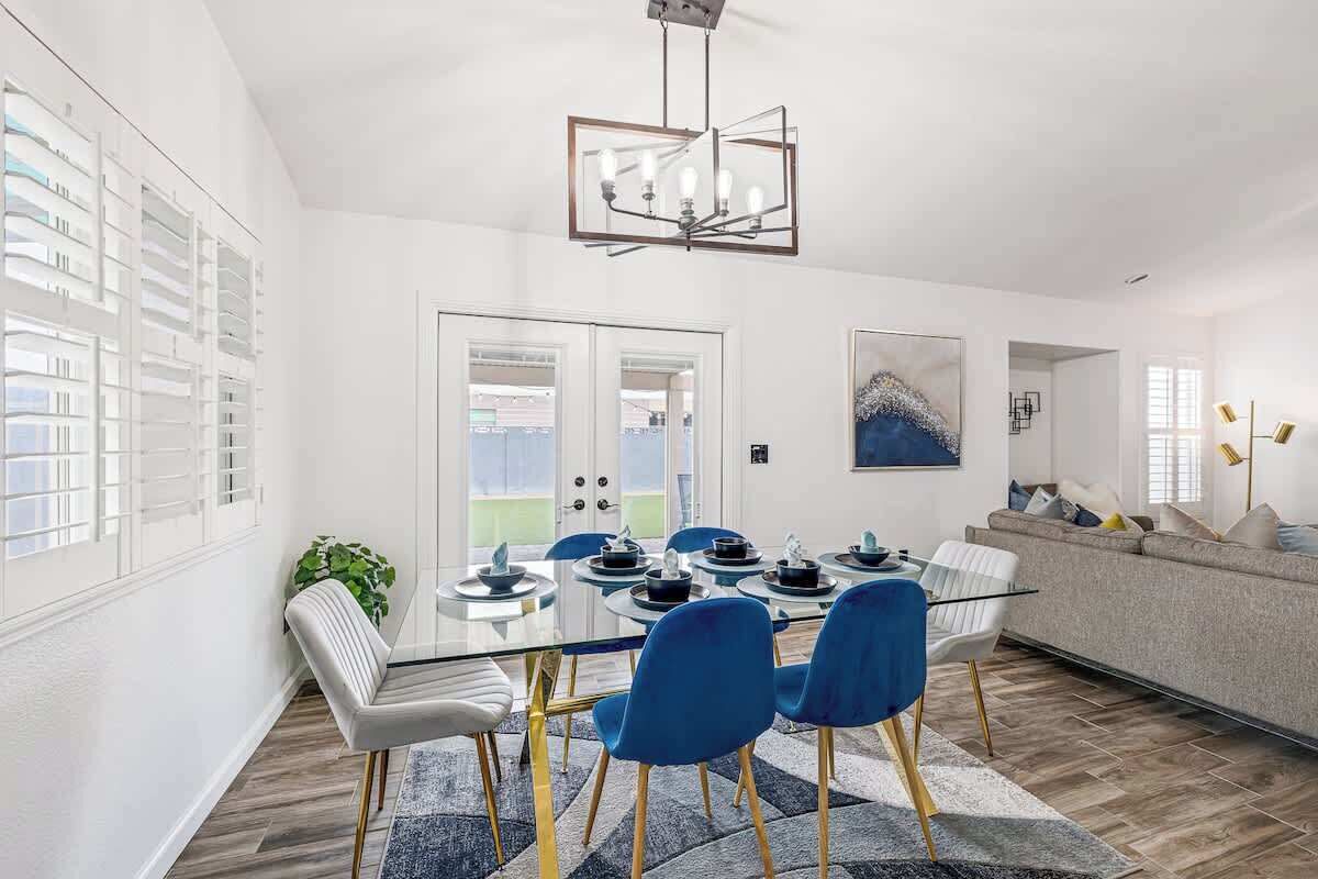 A modern dining area with a glass table, blue chairs, and a chandelier.