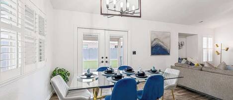 A modern dining area with a glass table, blue chairs, and a chandelier.