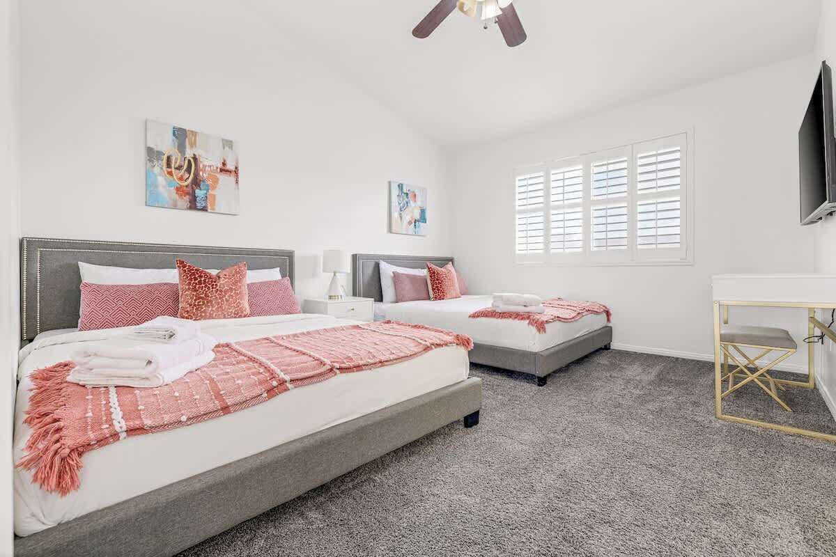Une chambre avec deux lits, un ventilateur de plafond, un bureau et des œuvres d’art accrochées aux murs.