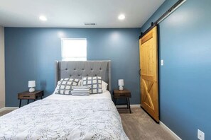 A bedroom with a large bed, two bedside tables, a window, and a wooden wardrobe.