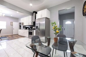 A modern kitchen with white cabinets, stainless steel appliances, and a glass dining table with chairs.