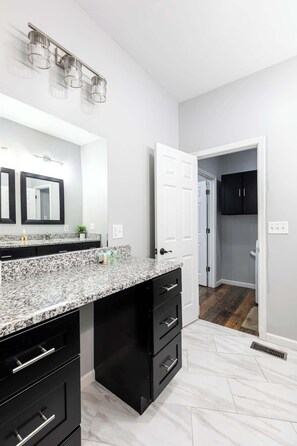 A modern bathroom with a granite countertop, black cabinetry, and a large mirror.