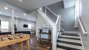 Ein geräumiges Wohnzimmer mit Tischfußball, einer Treppe und einem an der Wand befestigten Flachbildfernseher.