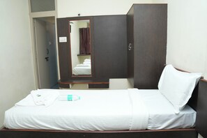 A single bed with white bedding, a wooden wardrobe, a mirror, and a small table with a bottle. - The Vishnu Residency (Chikkamagaluru)