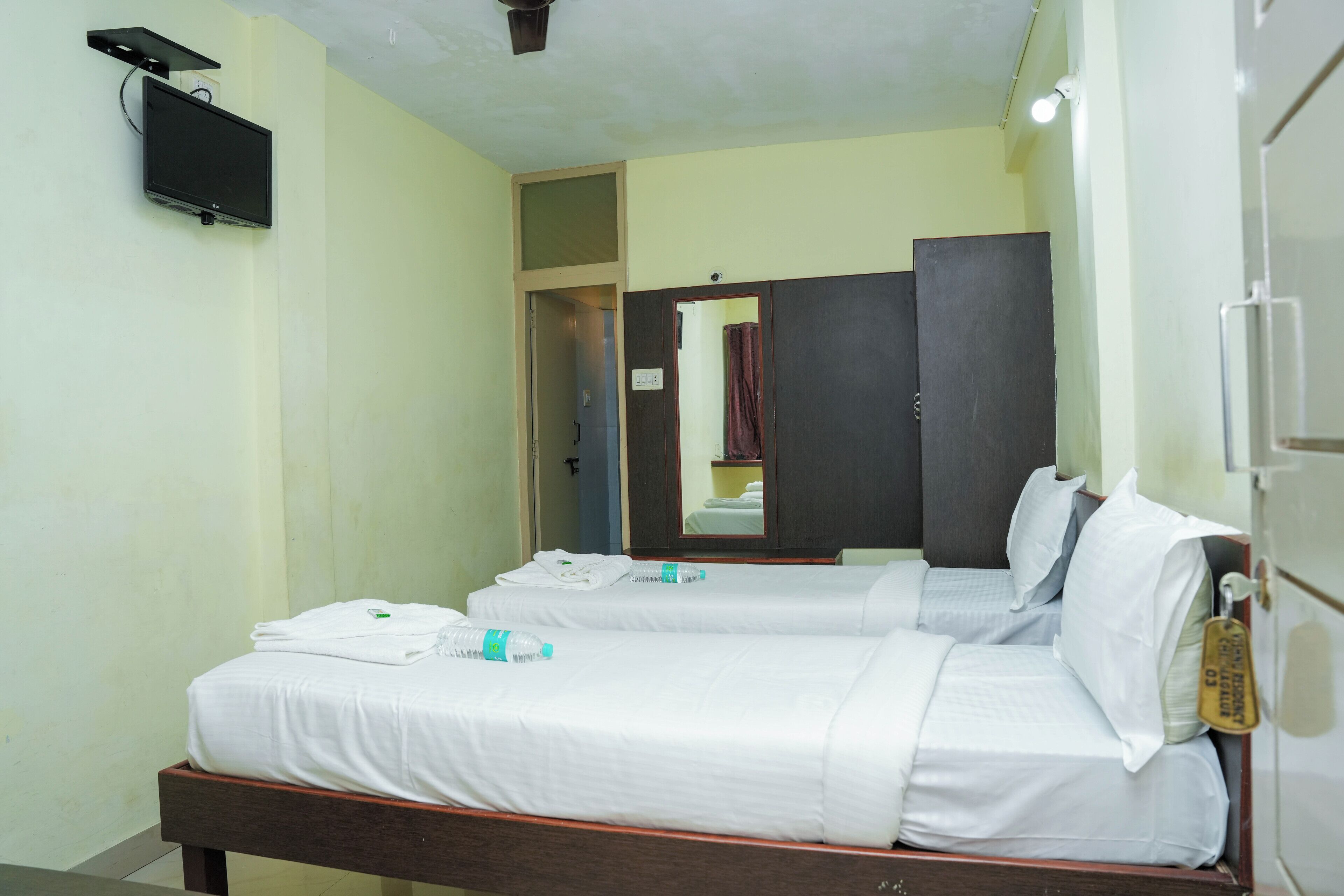 A hotel room with two single beds, a flat-screen TV mounted on the wall, and a mirror above the beds.