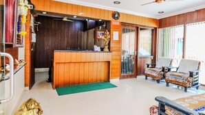 A reception area with a wooden reception desk, two armchairs, a ceiling fan, and a green carpet. - The Vishnu Residency (Chikkamagaluru)
