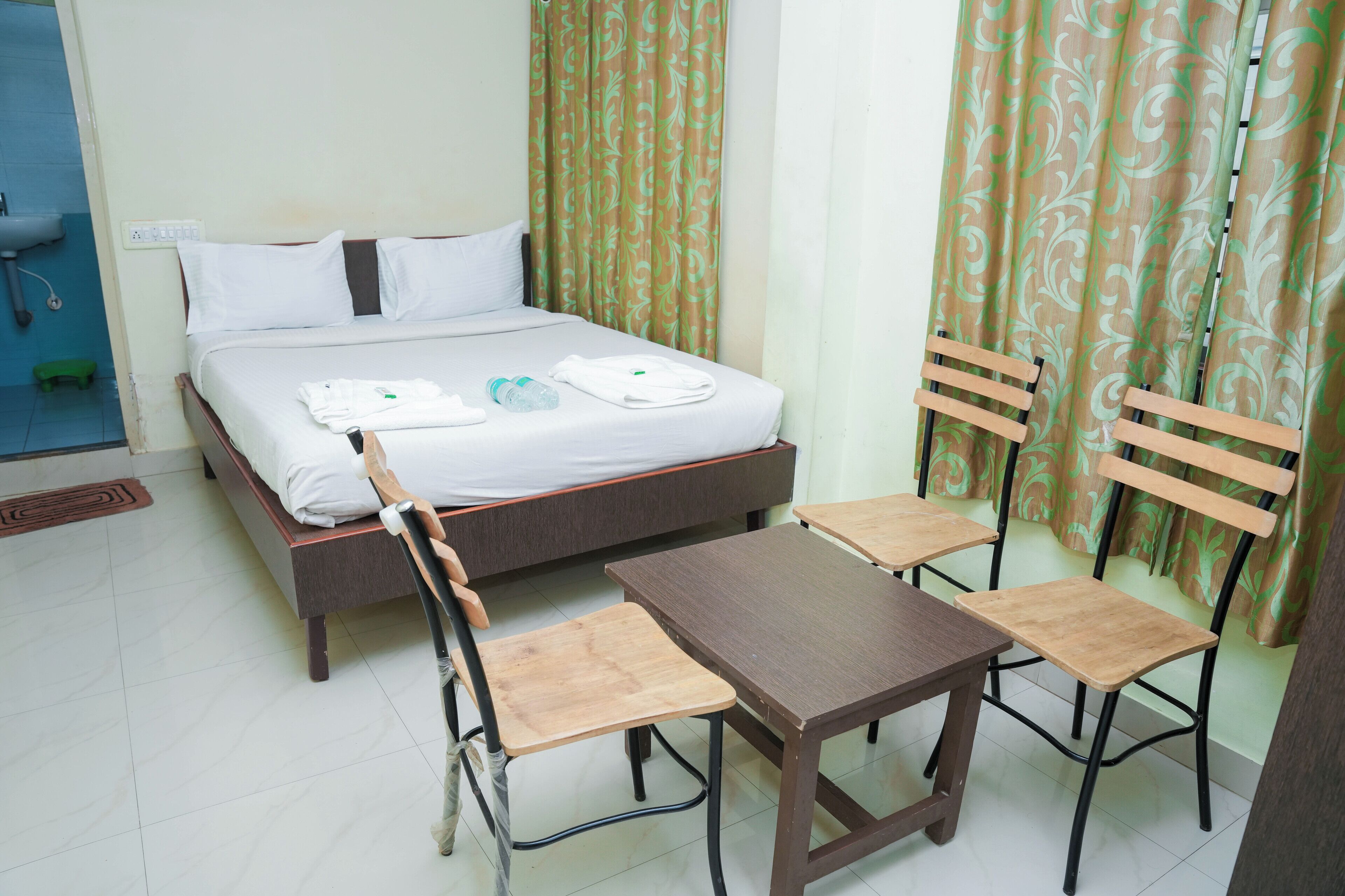 A hotel room with a bed, a table, and four wooden chairs.