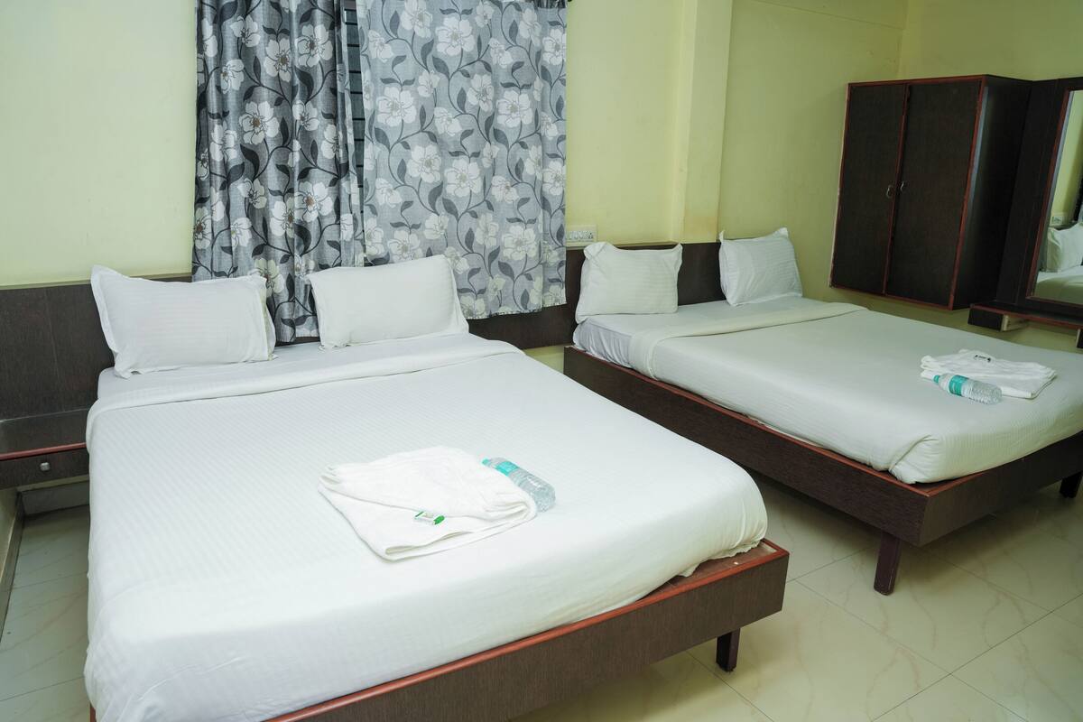 A hotel room with two beds, each with white linens and pillows, a wooden wardrobe, and a floral curtain.