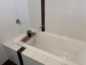 Et moderne badeværelse med et badekar, en træhylde med en potteplante, og en bøjle til håndklæder.