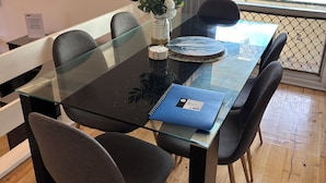 Ein moderner Essbereich mit einem Glastisch, schwarzen Stühlen, einer Blumenvase und einem Notizbuch auf dem Tisch.