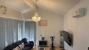 Ein modernes Wohnzimmer mit einer schwarzen Couch, einem Glastisch, einer Chandelierleuchte, einem Fernseher und einem Kamin.