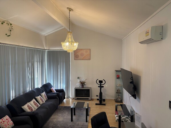 A modern living room with a black sofa, a glass coffee table, a chandelier, a TV, and a fireplace. - Sunflower Homes Classy and Cozy (Para Hills)