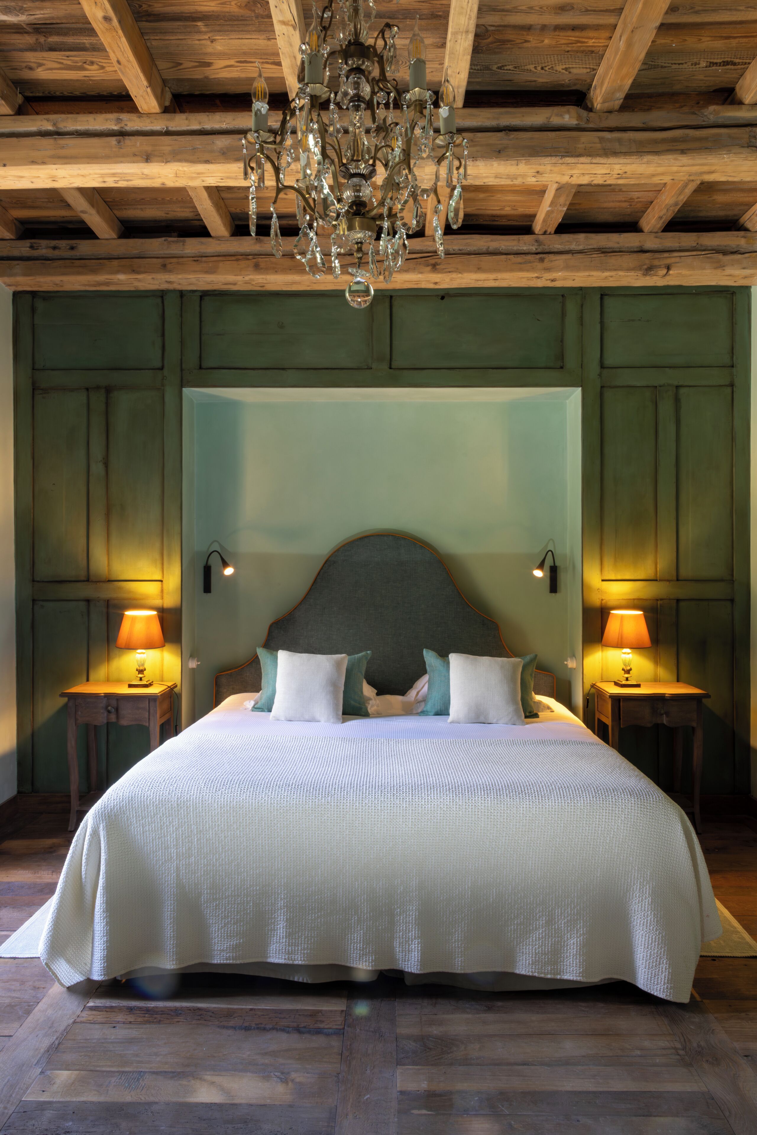 Una cama grande con cabecera de madera, dos lámparas de noche y un candelabro.