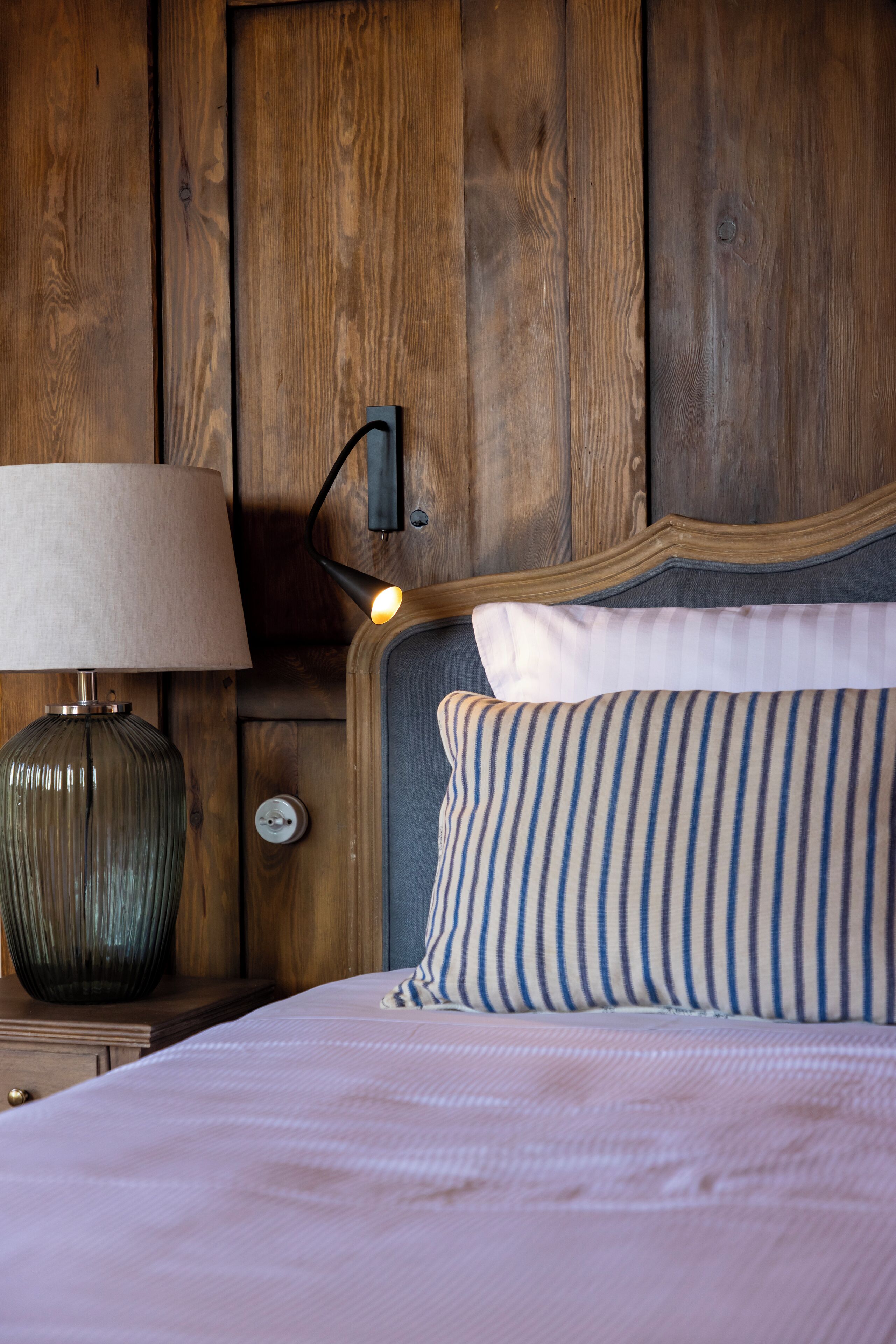 A wooden headboard with a lamp and a striped pillow on a bed.