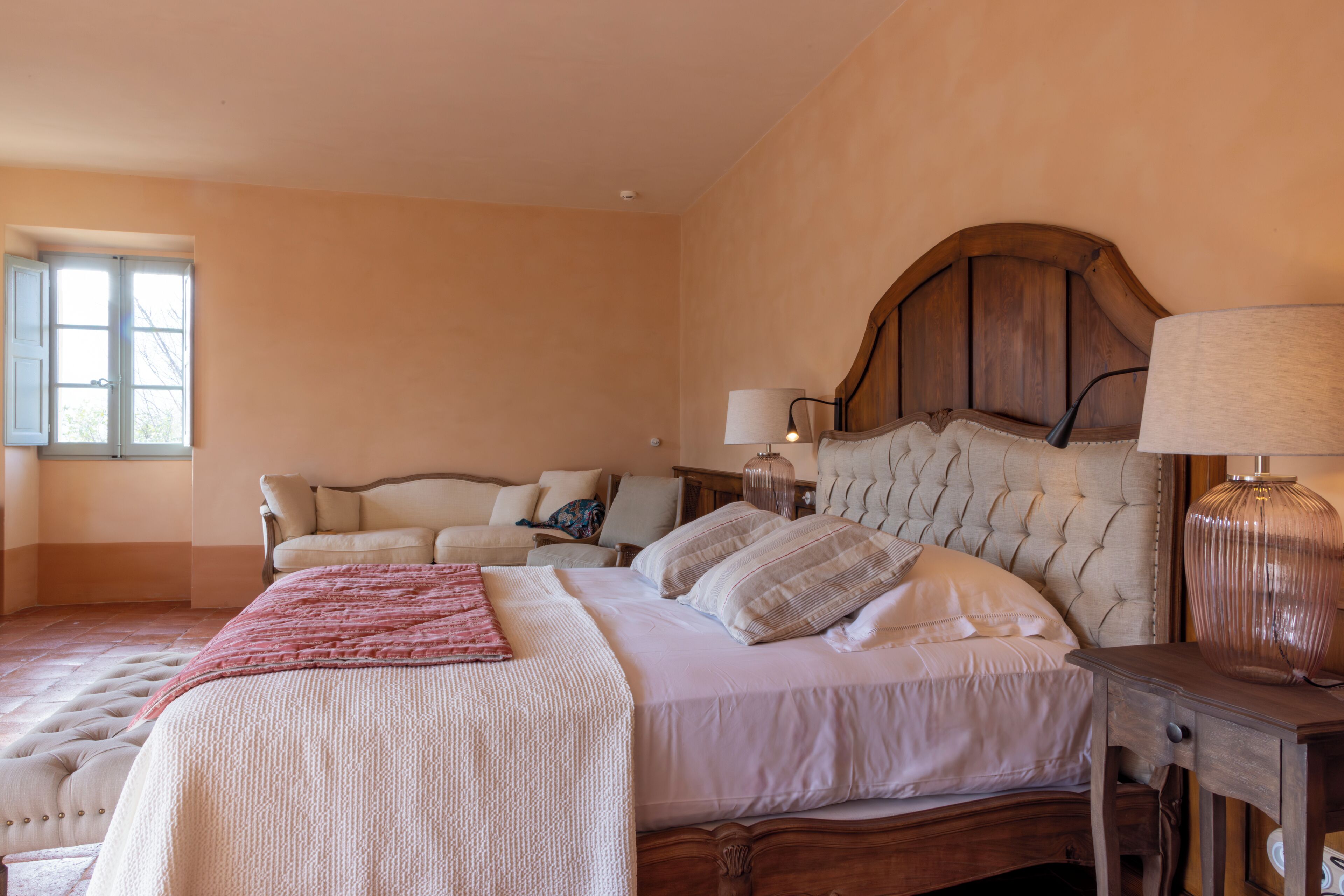 Un dormitorio con una cama grande, un sofá más pequeño y una mesita de noche con una lámpara.