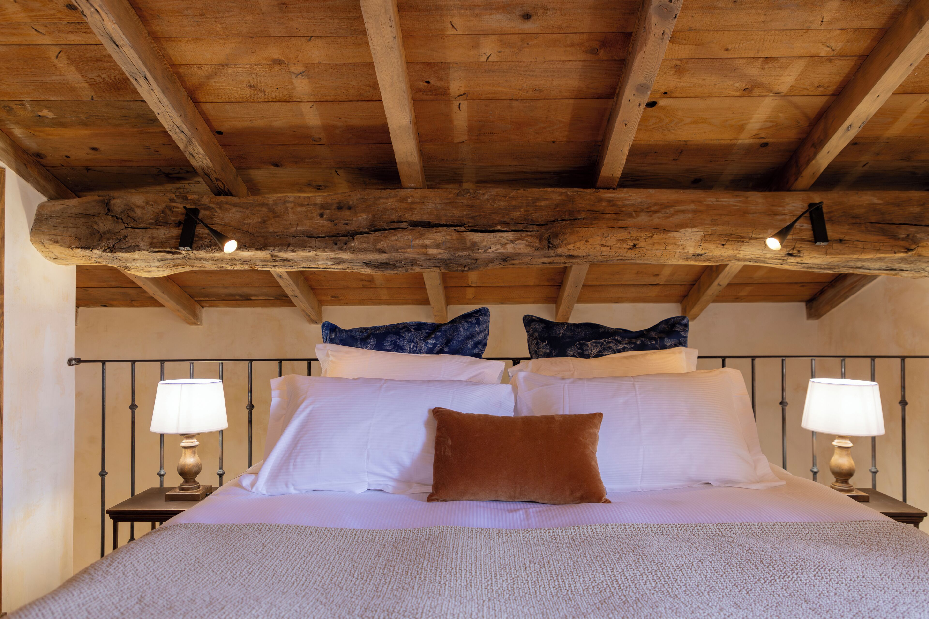 A bedroom with a wooden ceiling, a bed with white linens, two bedside tables with lamps, and decorative pillows.