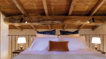 A bedroom with a wooden ceiling, a bed with white linens, two bedside tables with lamps, and decorative pillows.