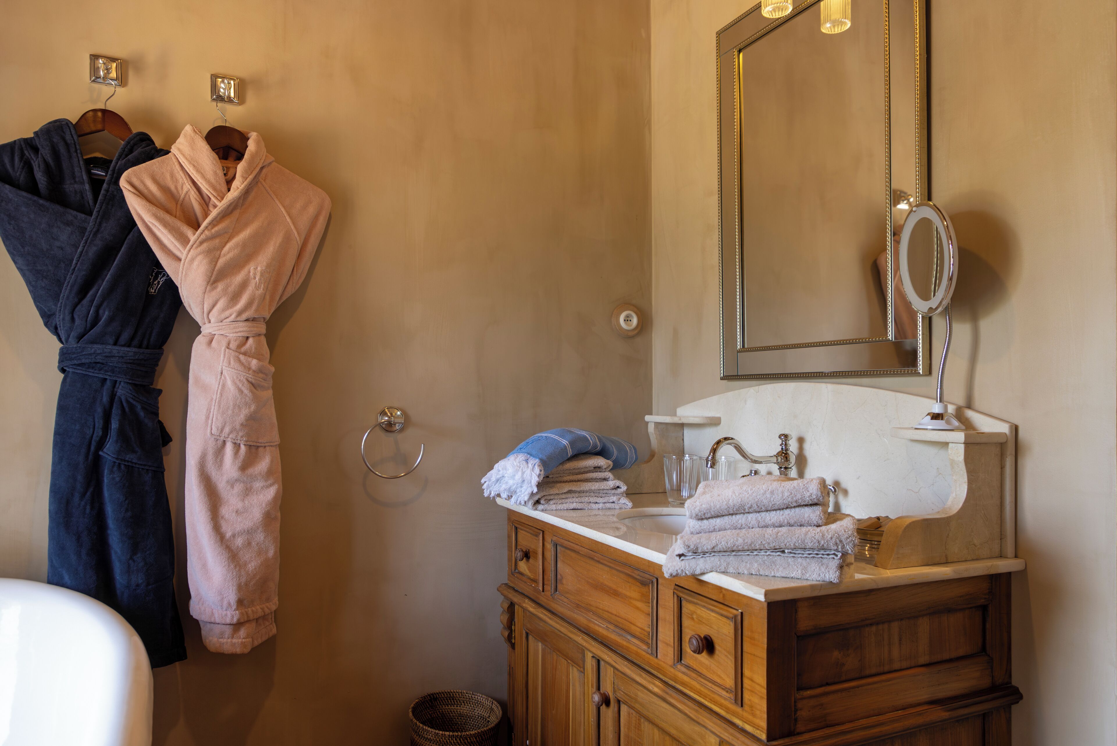 Un baño con tocador de madera, un espejo y dos albornoces colgados en la pared.