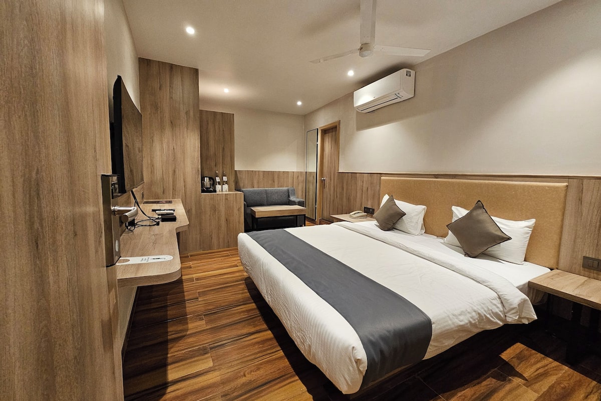 A modern hotel room with a large bed, a desk, a sofa, and a ceiling fan.