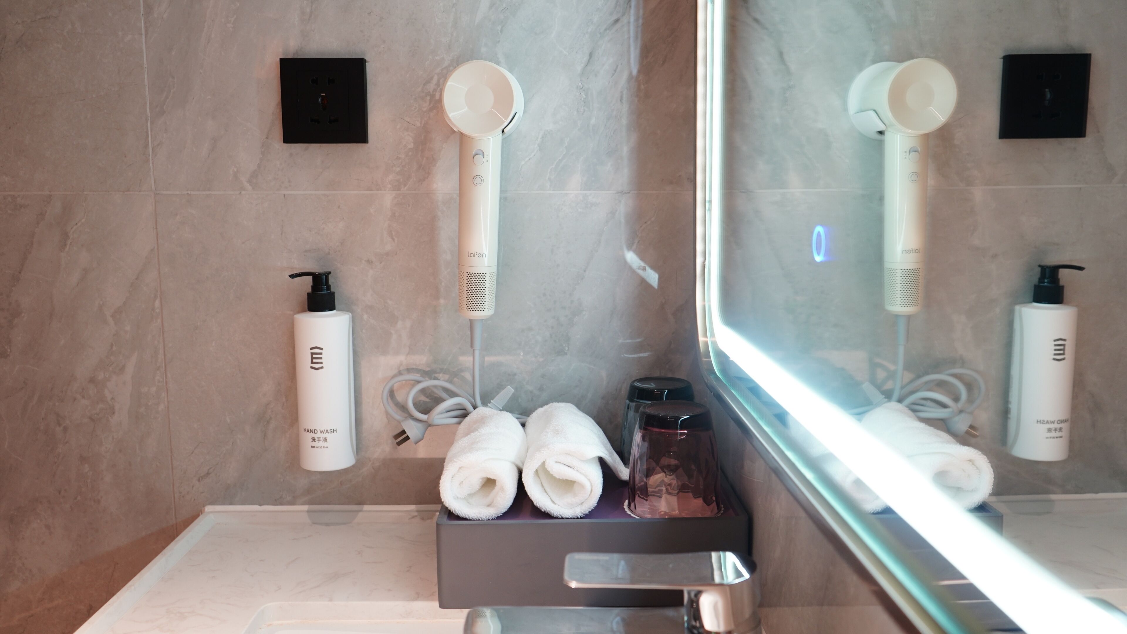 A modern bathroom with a large mirror, two towel racks, a hand wash station, and a glass shower enclosure.