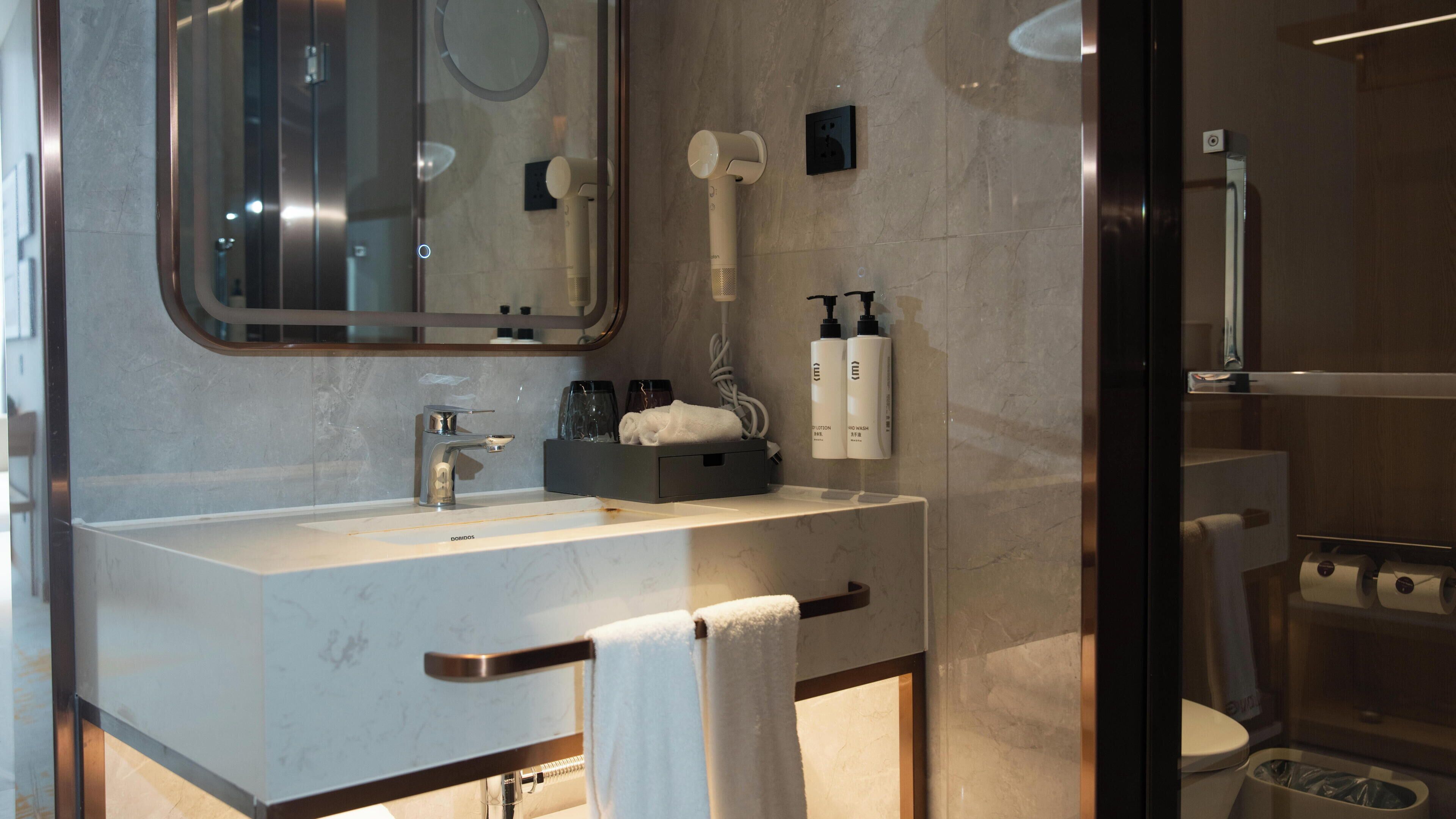 A modern bathroom with a marble sink, a towel rack, a mirror, and a shower area.