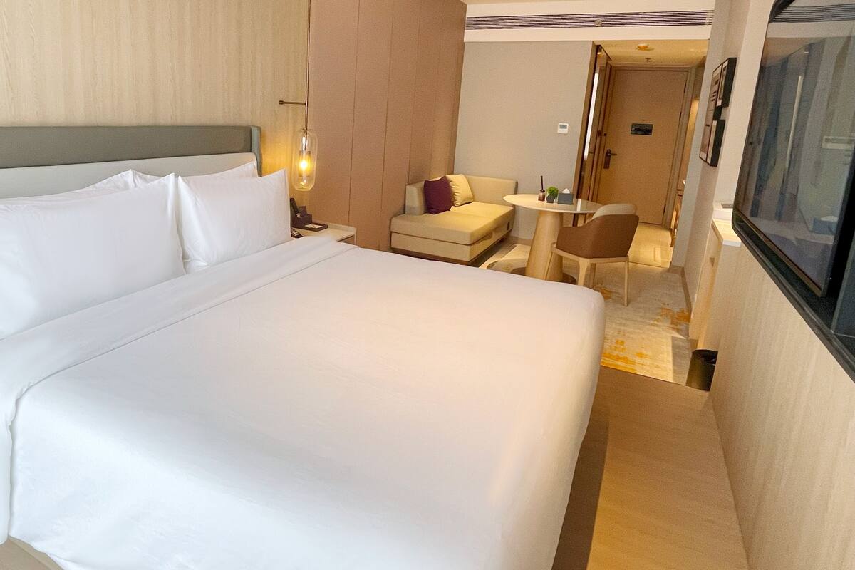 Quarto de hotel com uma cama grande, uma mesa pequena, uma cadeira e uma televisão.