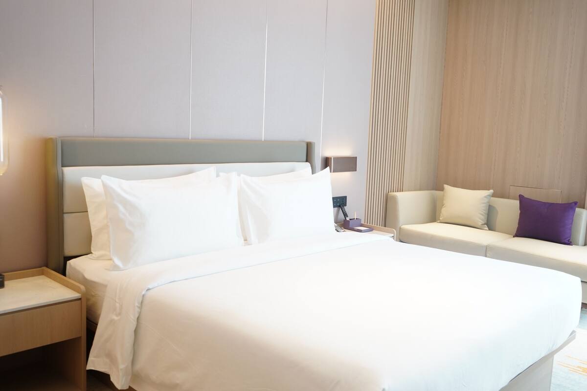 Quarto de hotel com uma cama grande, mesa de cabeceira, sofá e luminária na parede.
