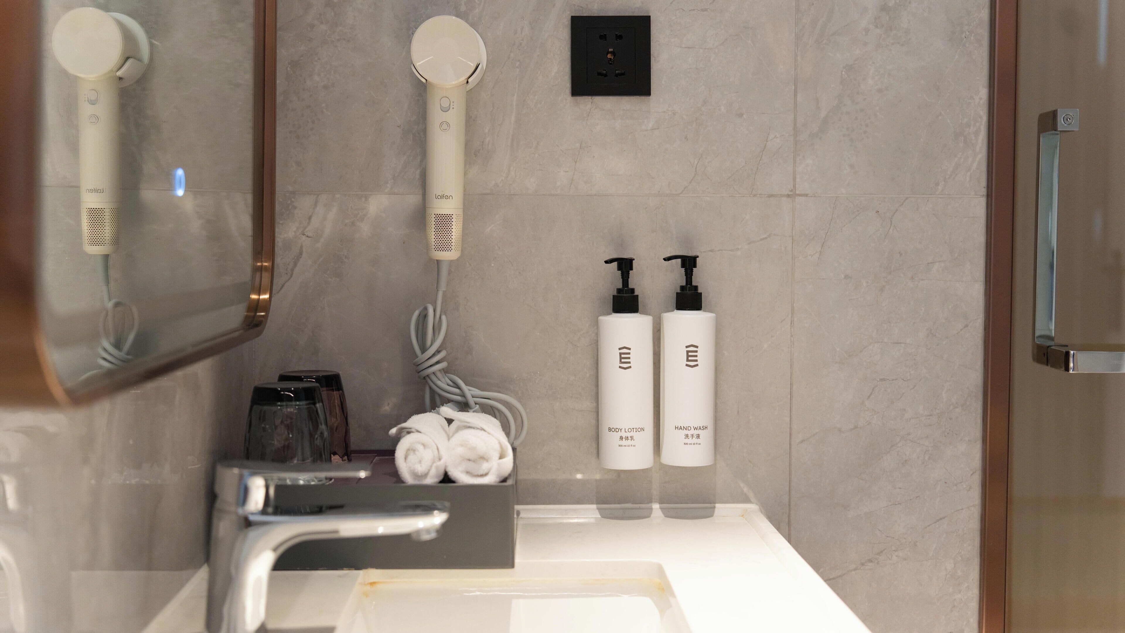 A bathroom with a mirror, a hairdryer, a towel, and two bottles of lotion.