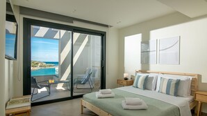 Quarto com uma grande porta de correr de vidro que dá para uma varanda, uma cama com várias almofadas, uma mesa de cabeceira e uma pequena mesa com abajur.