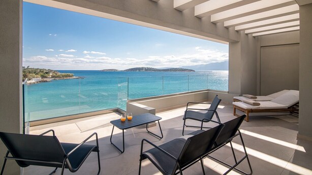 Uma varanda com vista clara para o mar, uma mesa com duas cadeiras e um espaço de estar com duas camas.