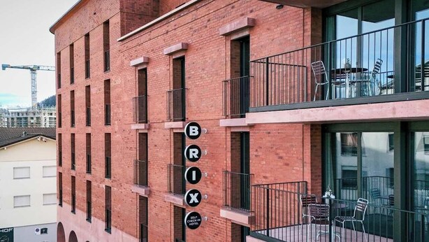 Un bâtiment en briques rouges, sur lequel on peut lire l’inscription « Brix Hotel », et un balcon doté de sièges pour l’extérieur.