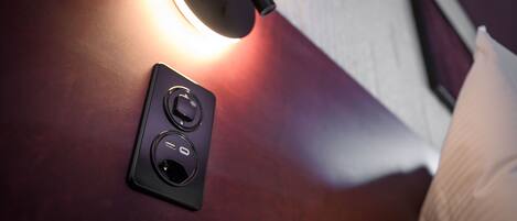 A wall-mounted control panel with buttons and a switch, a lamp casting light on the wall, and a pen on a surface.