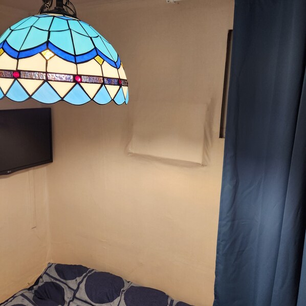 A room with a bed, a TV mounted on the wall, and a decorative stained glass lamp. - Hostel Hanil (Seoul)