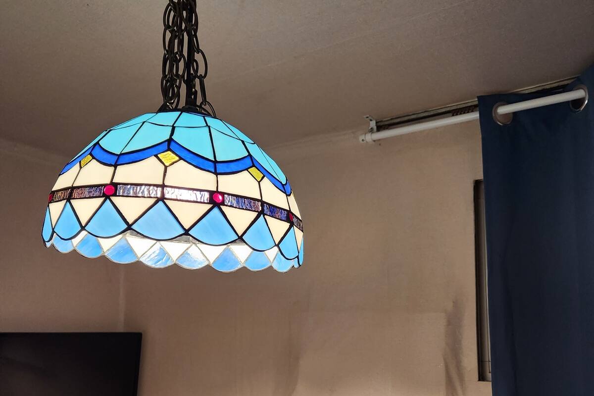 A room with a hanging stained glass light fixture, a flat-screen TV mounted on the wall, and a curtain rod with a blue curtain.