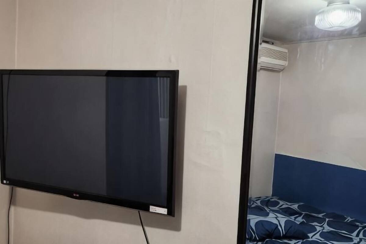A room with a mounted television, a bed with patterned bedding, and a ceiling fan.