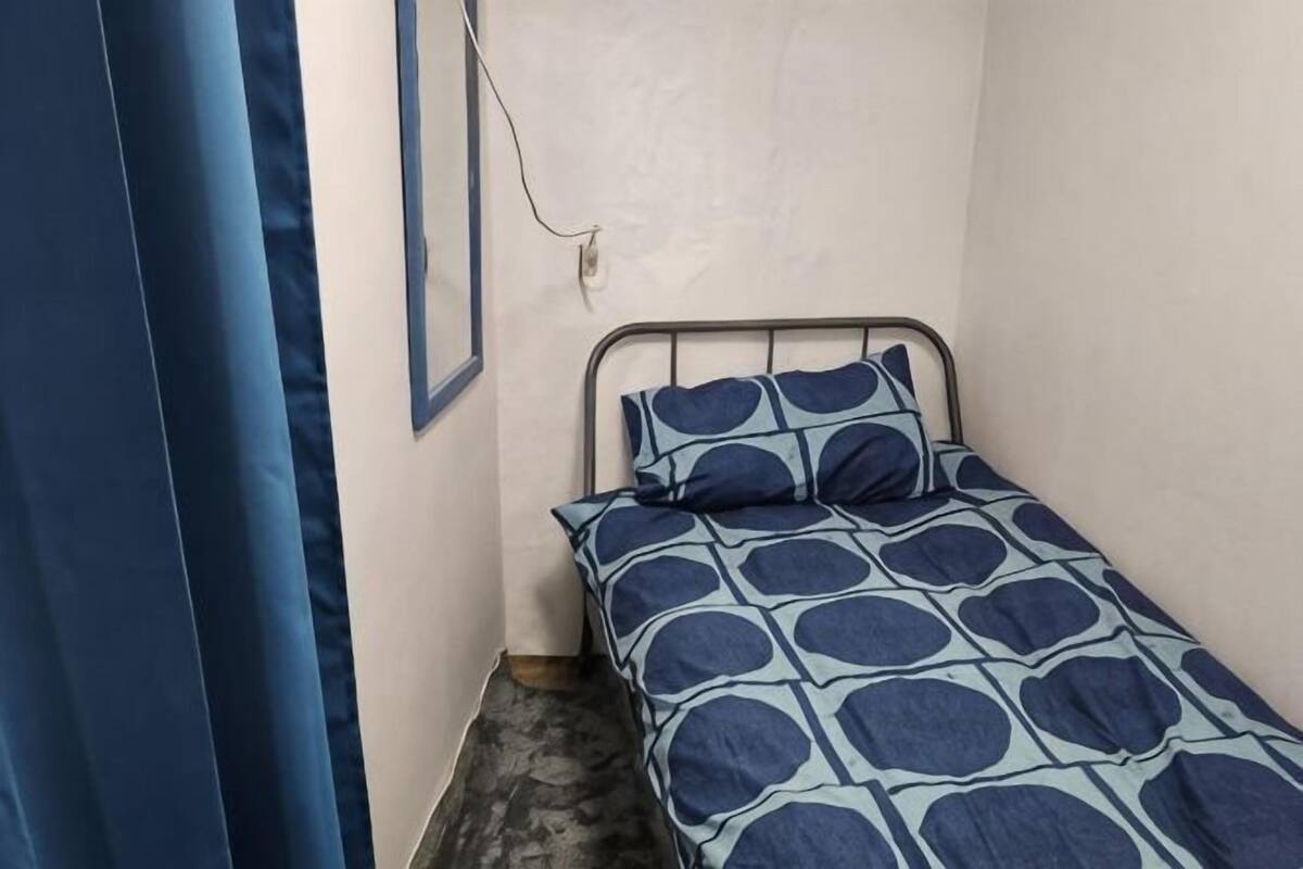 A small, single-bed room with a metal frame, a patterned bedspread, and a curtain on the left.