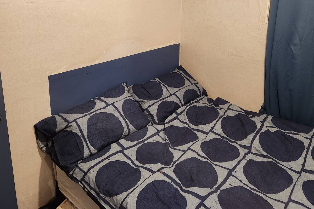 A small, single-bed room with a blue headboard and a patterned bedspread.