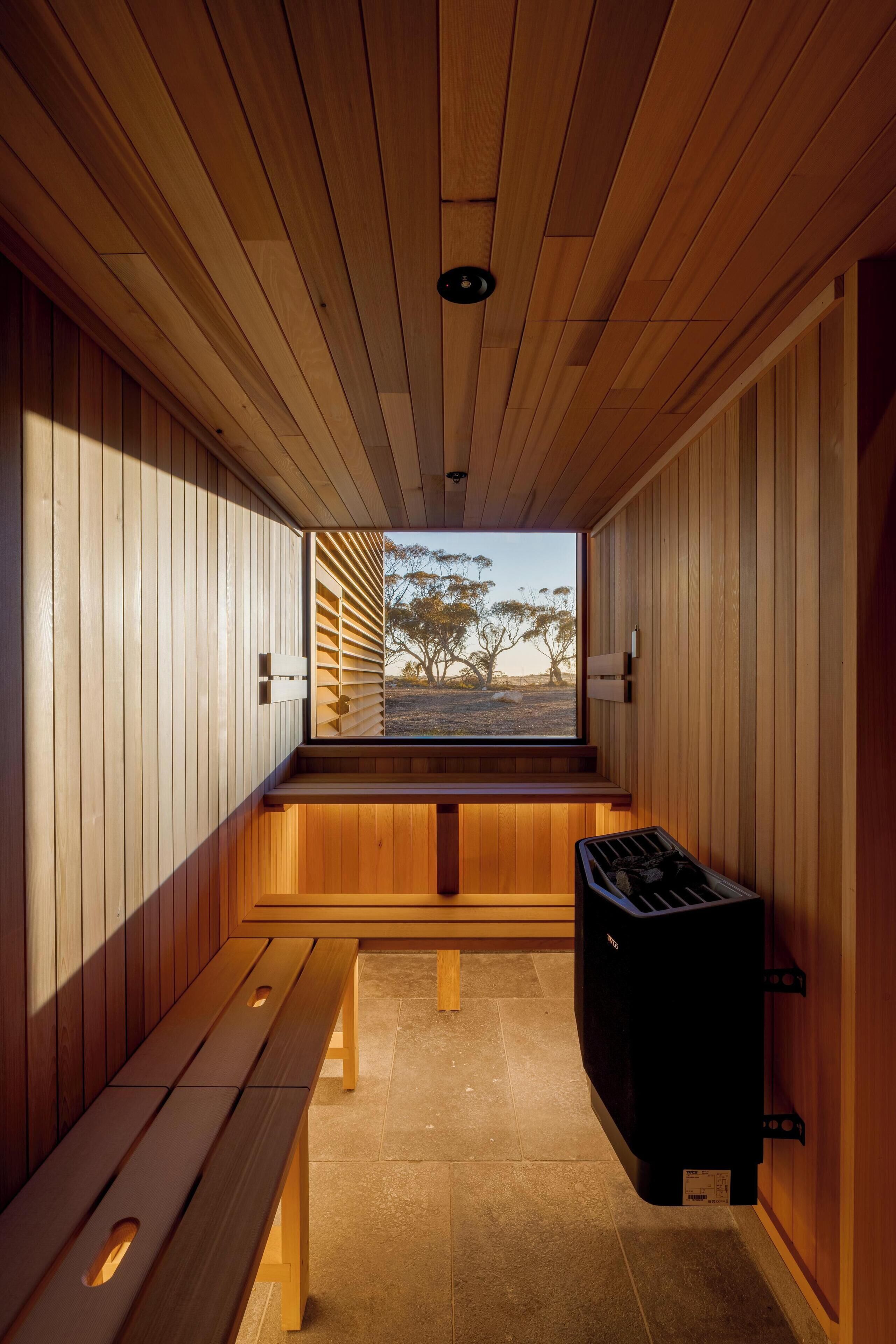 A sauna room with wooden walls, a bench, and a sauna heater.